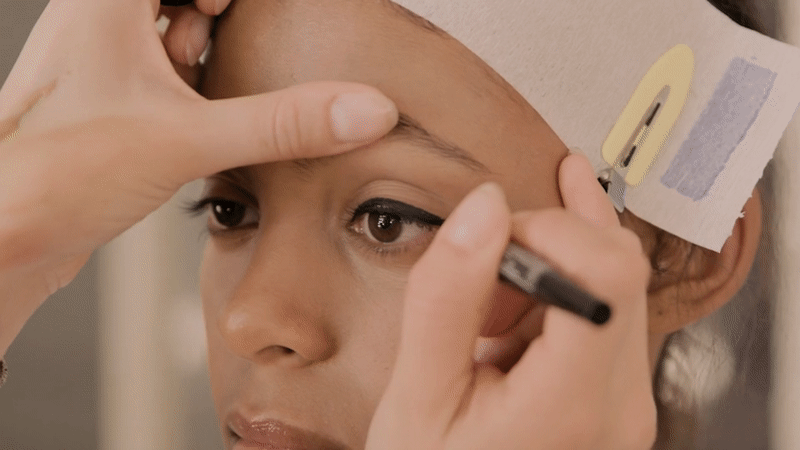 Animated GIF showing a makeup artist applying makeup to a model before a fashion show.