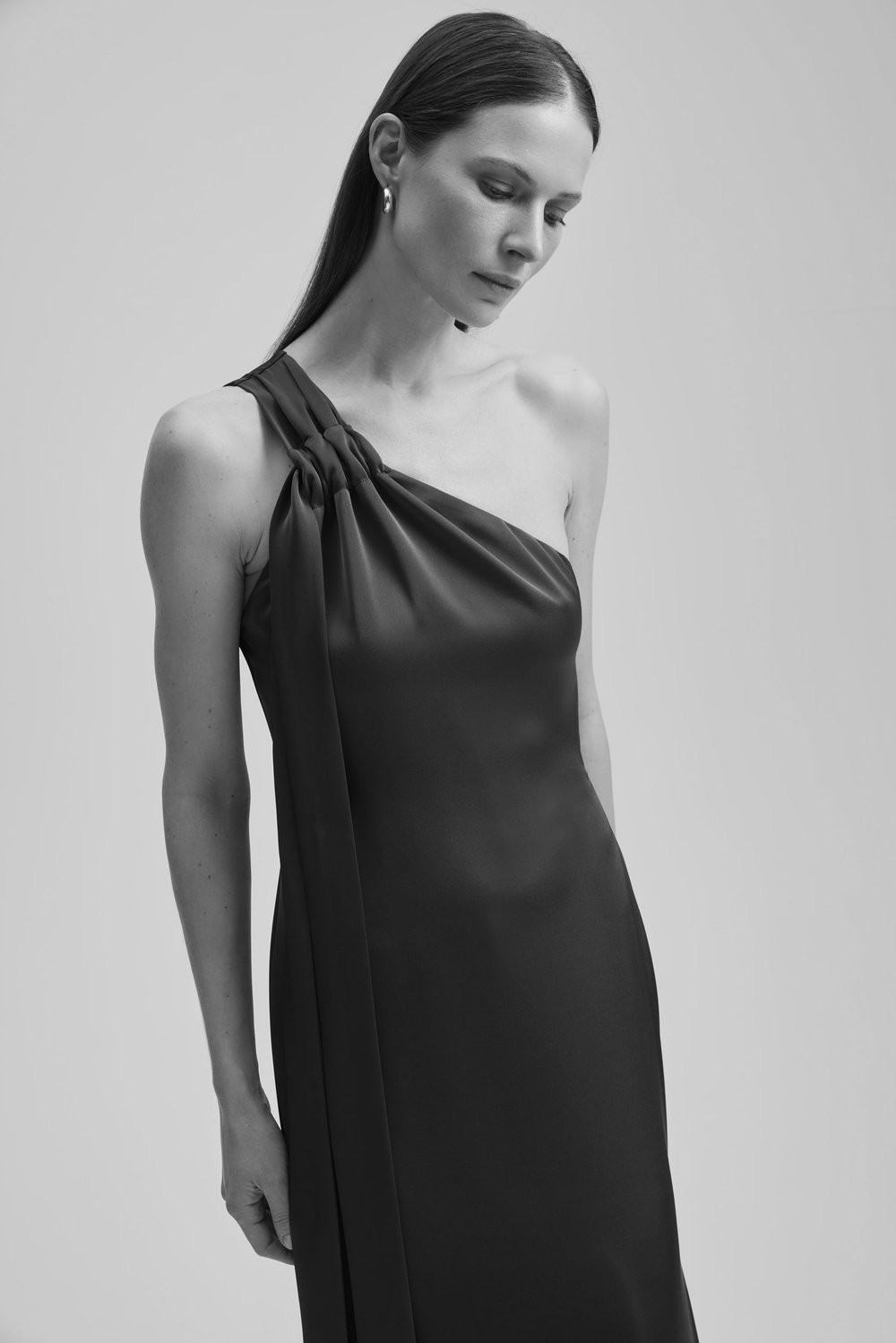 Black and white photo of a model in a studio, wearing a dark grey dress.